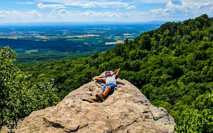 a student rests on a rock overlooking green forests on a backpacking trip for teens